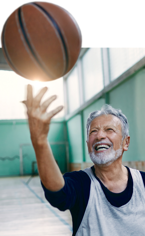 Senior spielt Basketball in der Halle Ein älterer Mann mit grauen Haaren genießt aktiv das Basketballspielen in einer Sporthalle.